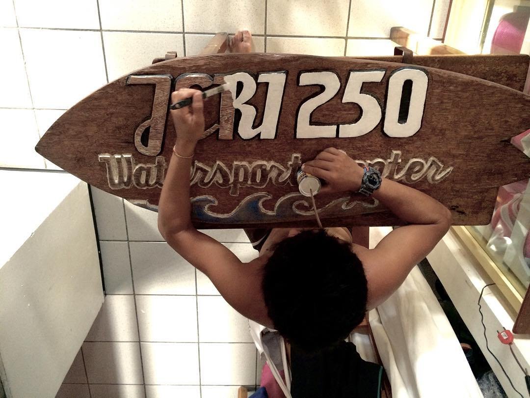 Edvan pintando à mão a placa de madeira da própria escola de windsurf